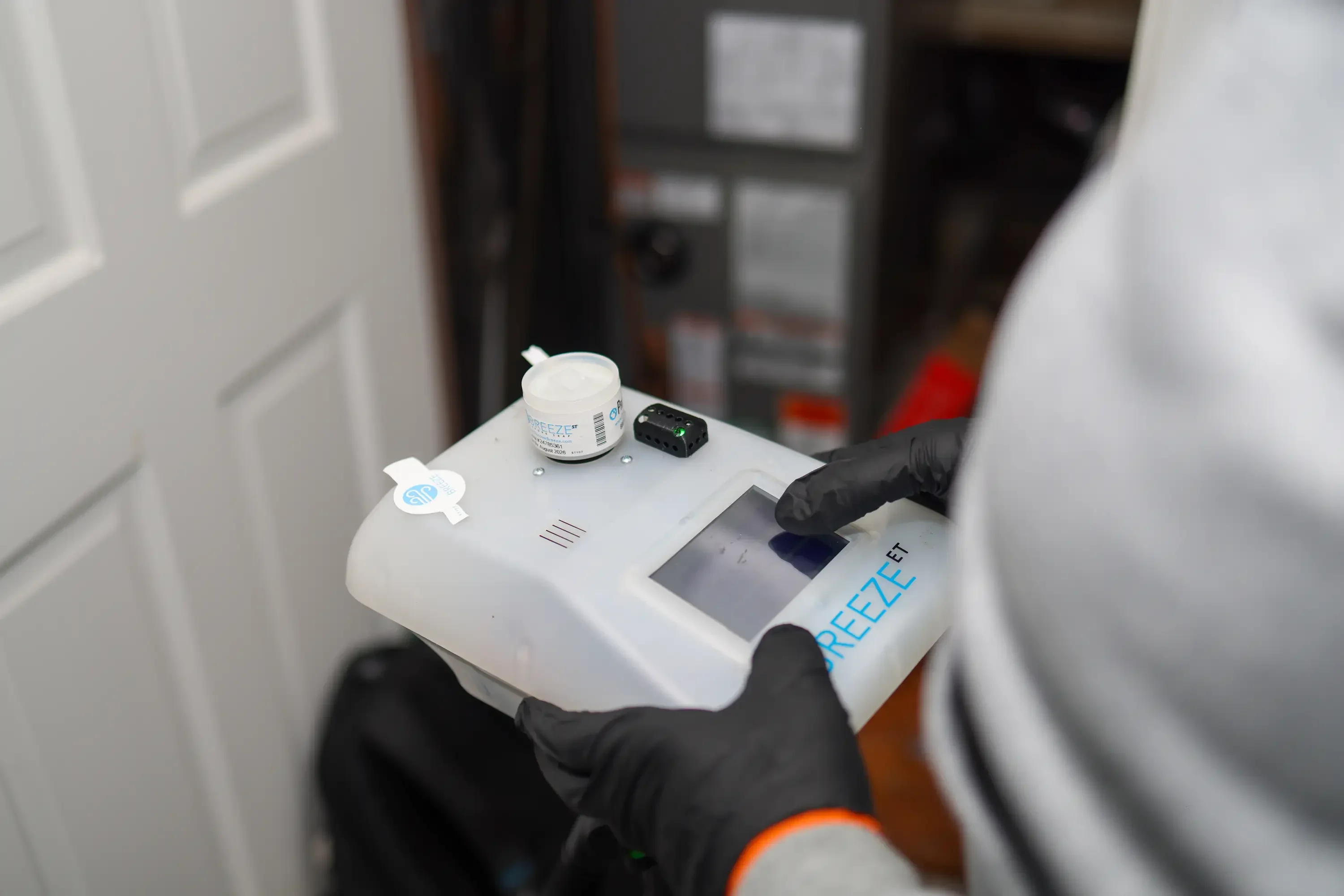 Technician in protective gear holding air quality testing equipment during home inspection