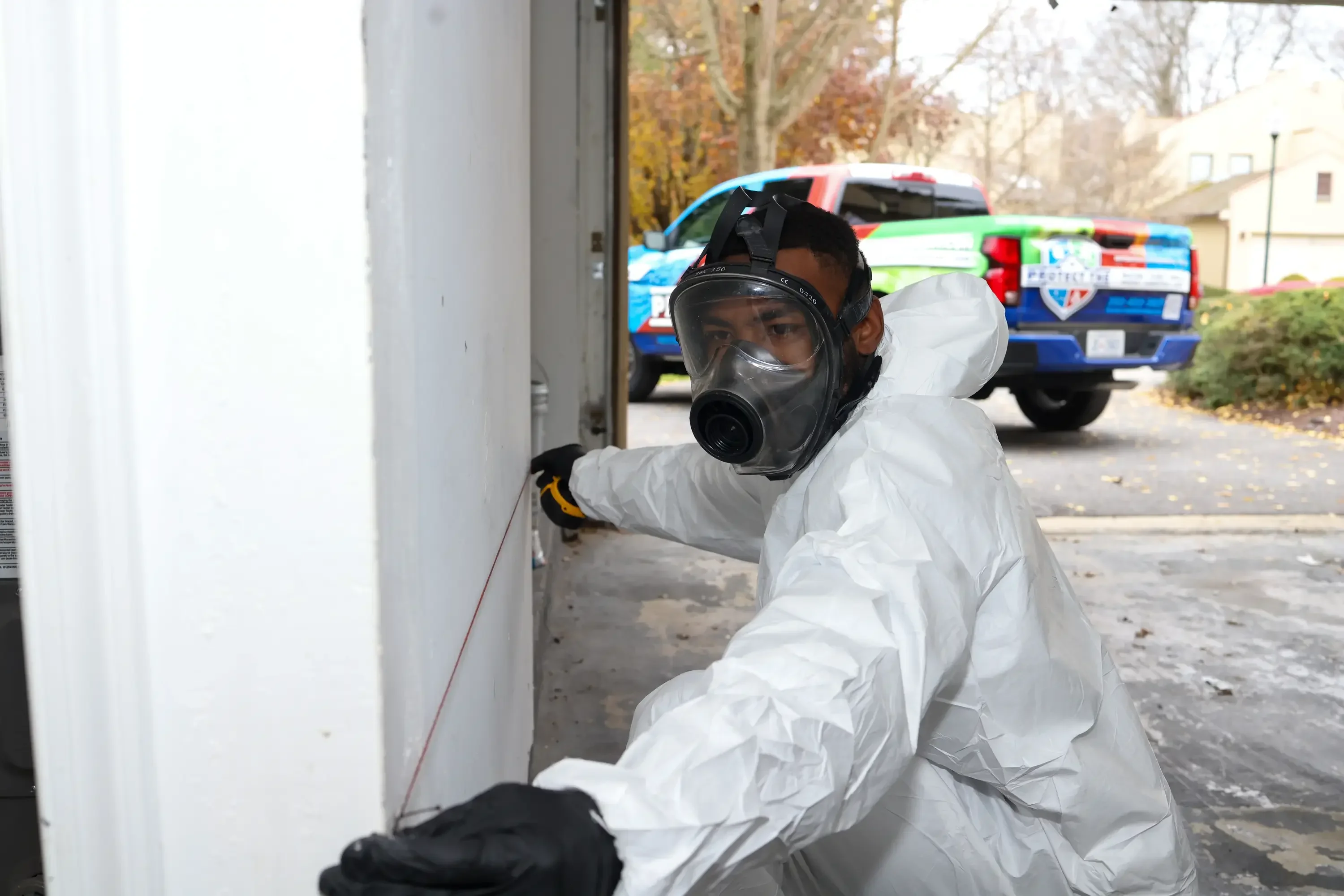 Technician in white hazmat suit and respirator conducting environmental assessment of building exterior