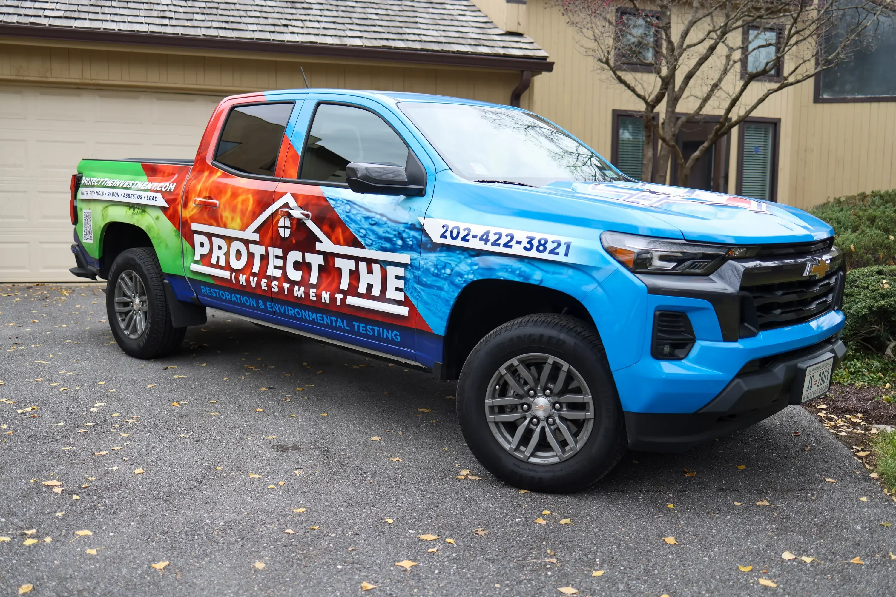 Blue pickup truck with custom wrap displaying Protect The Investment branding and contact number