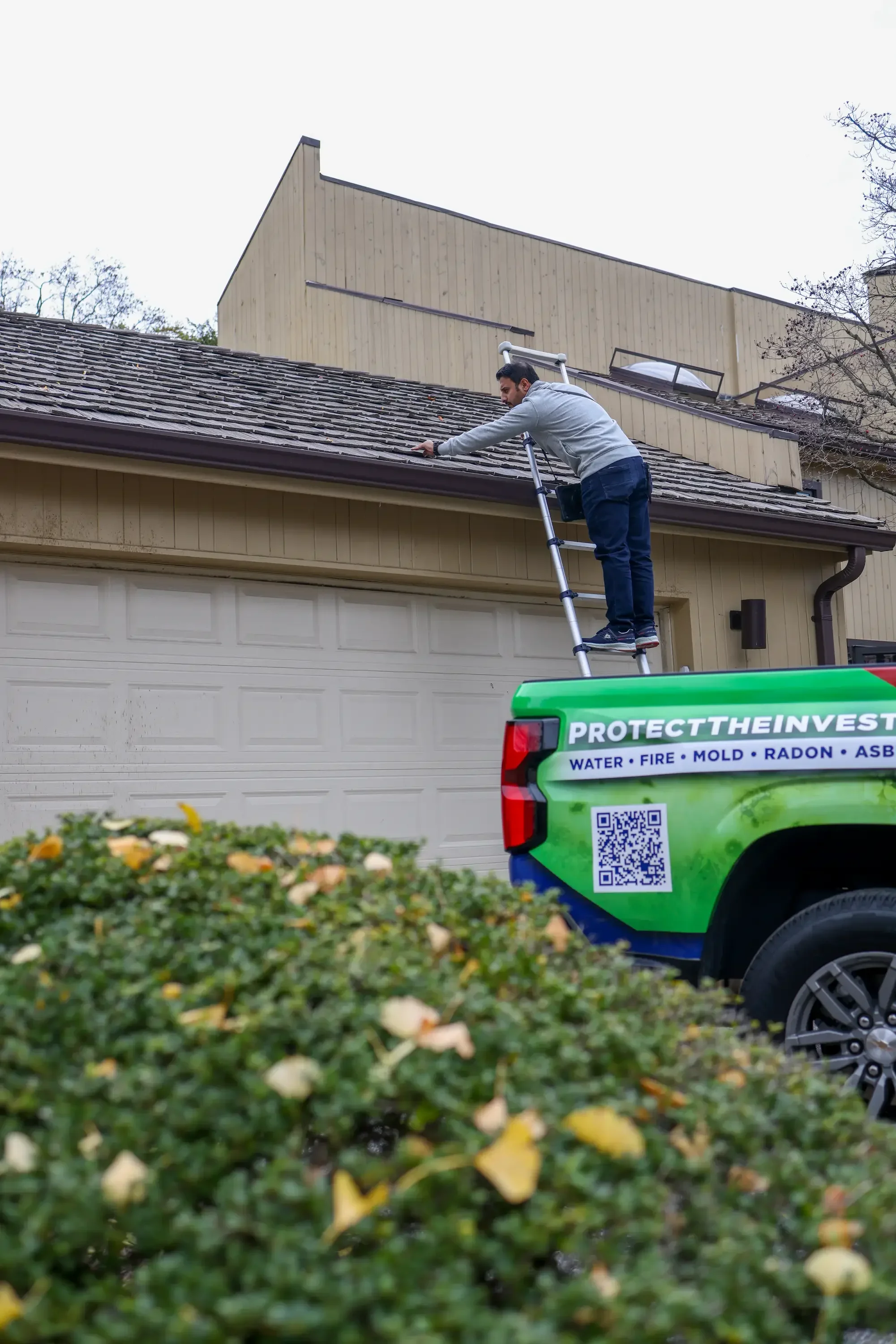 Inspector on ladder examining residential roof and exterior during home inspection