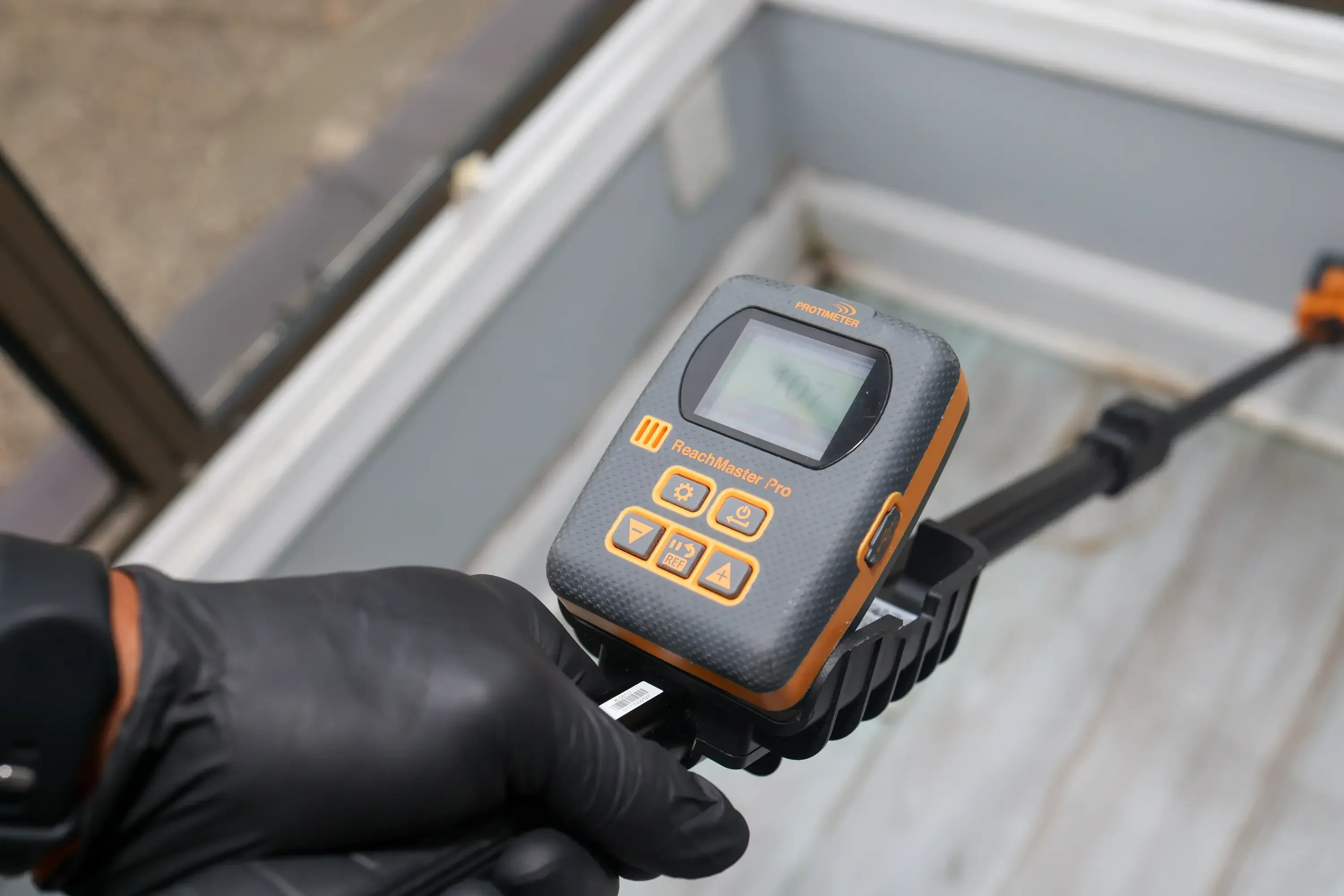 Technician holding ReachMaster Pro moisture meter over white inspection container