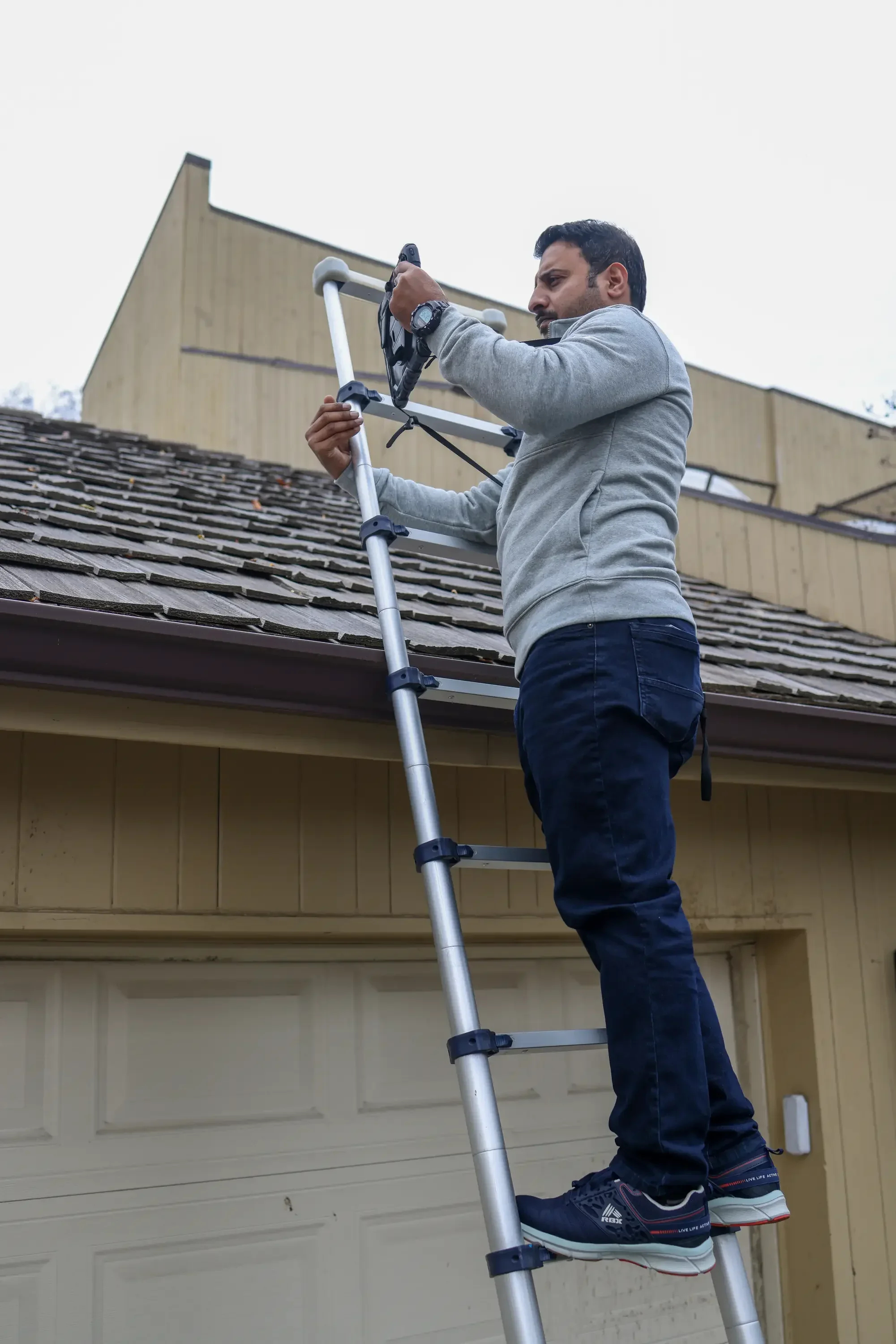 Inspector on ladder examining residential roof shingles and structure during home inspection