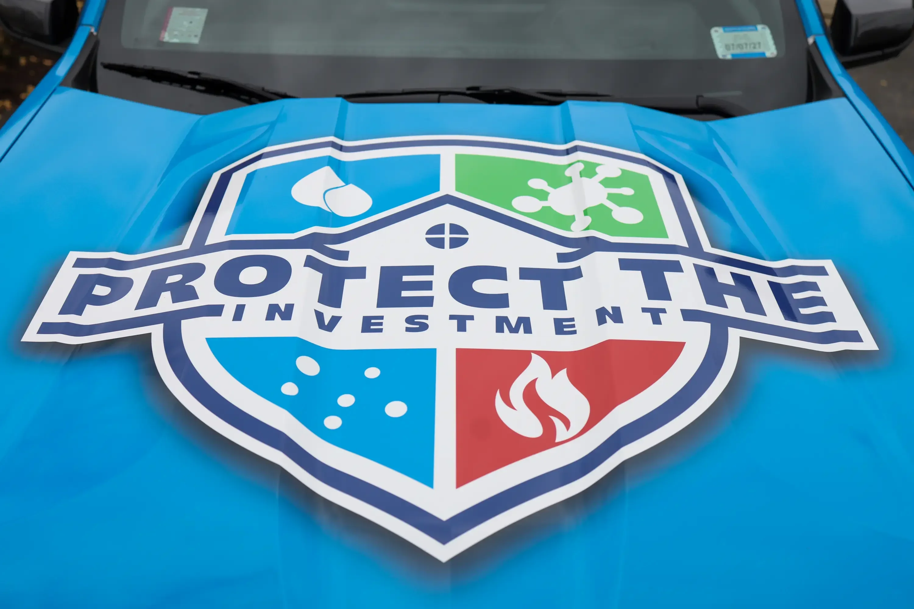 Blue vehicle wrap with Protect The Investment shield logo on hood
