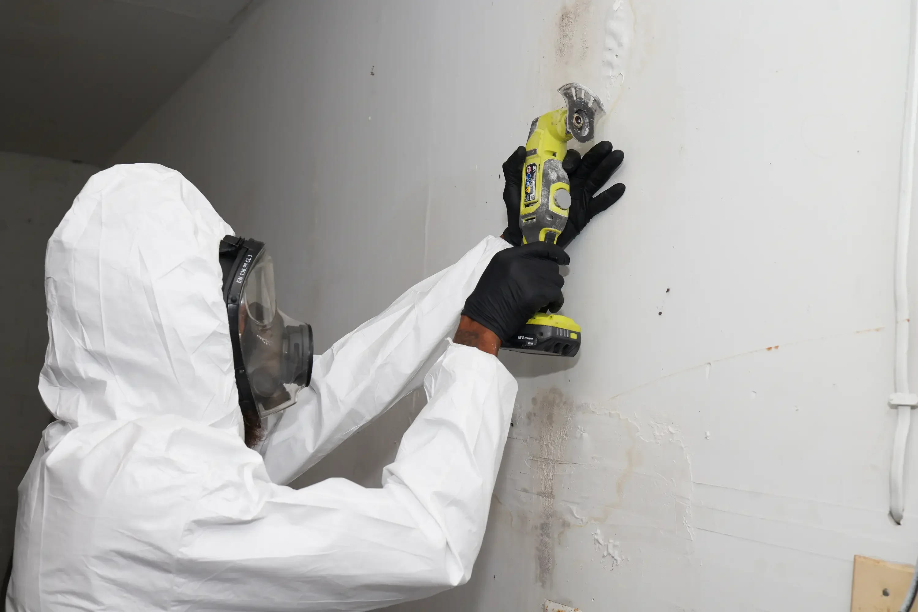 Technician in protective suit using power tool to remediate mold on interior wall
